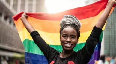 mulher sorrindo enquanto segura uma bandeira LGBT.