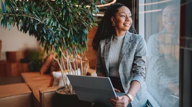 mulher empreendedora olhando pela janela sorrindo com notebook no colo.