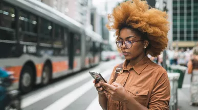 Mulher olha o celular, com um ônibus ao fundo