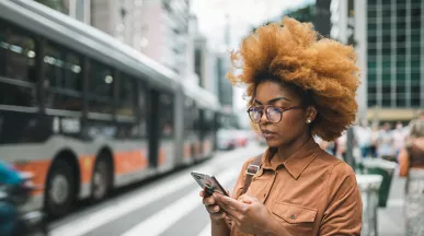 mulher usando o celular enquanto onibus do sistema de transporte de são paulo passa ao lado.