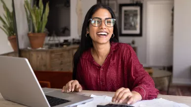 mulher sorrindo enquanto vê algo em notebook.