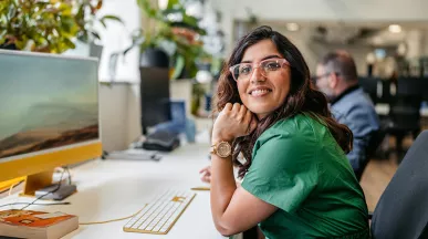 mulher sorrindo para a câmera enquanto trabalha em frente a computador.