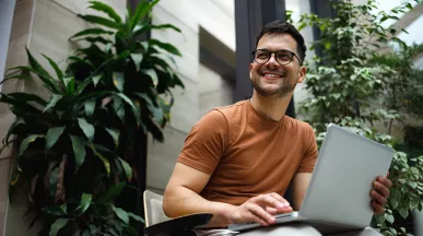 homem usando notebook no colo enquanto sorri.