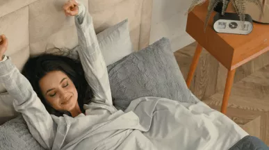 A imagem mostra uma mulher em uma cama, se espreguiçando ao acordar 