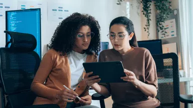 duas mulheres discutindo sobre algo enquanto olham tablet.
