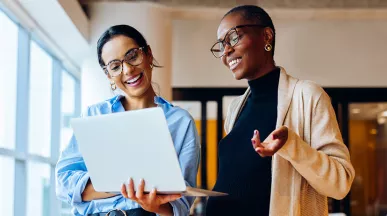 duas mulheres conversando animadamente enquanto veem algo em computador.