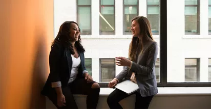 Foto mostra duas pessoas conversando em uma sala de reunião