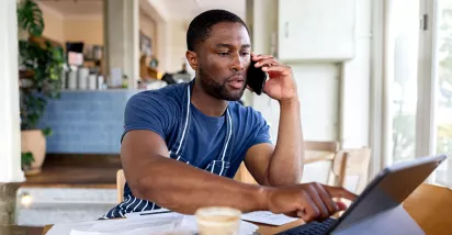 dono de empresa falando no telefone enquanto usa notebook.