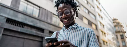 Homem confere o celular na rua despreocupado: ele tem seguro Pluxee