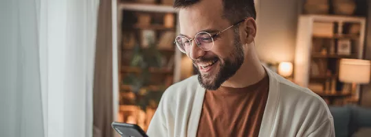 Na foto, um homem olha para o seu celular