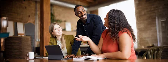 Foto mostra três colegas de trabalho conversando sobre uma tarefa