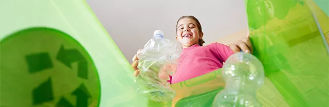 Foto mostra uma criança jogando uma garrafa plástica no lixo correto