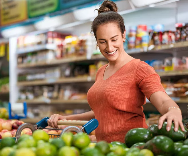 Mulher escolhe alimentos frescos no supermercado. Ela vai pagar a compra com vale-alimentação.