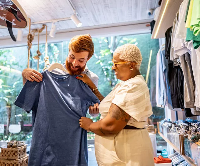 Homem escolhe camiseta azul em loja que aceita o vale-presente Pluxee Gift.