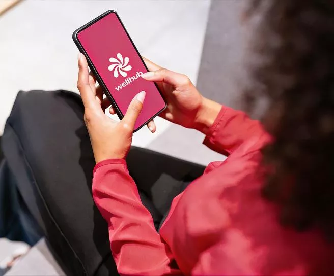 Pessoa segurando um smartphone exibindo a tela inicial do aplicativo Wellhub.