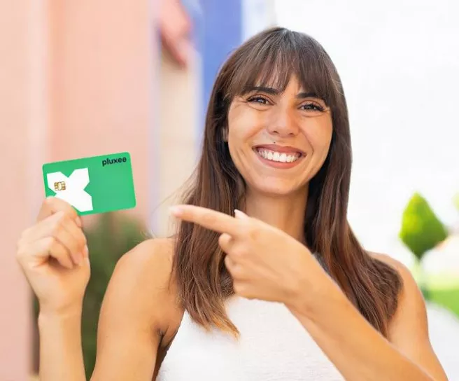 Pessoa segurando e apontando para um cartão verde Pluxee em ambiente externo.