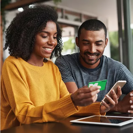 Duas pessoas em ambiente interno usando cartão Pluxee Multi, smartphone e tablet em cenário de compra digital