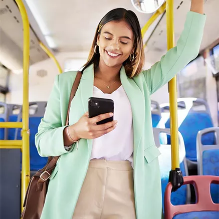 Mulher em pé dentro de um ônibus, segurando a barra de apoio e usando o celular durante o trajeto.